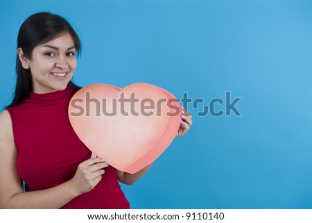 A pretty young woman holding a large valentine taken on a blue background with copy space.
