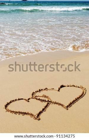 couple drawing a heart on wet golden beach sand