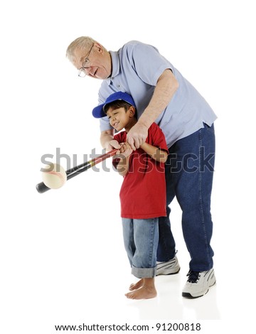 A senior and his preschool grandson working together to successfully bat a baseball.  On a white background.
