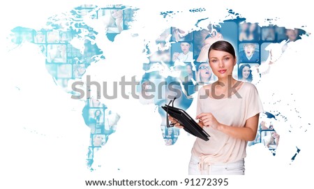Portrait of young pretty woman working on modern tablet computer while standing against big virtual map with photo of her friends or colleagues