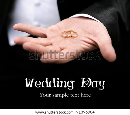 Groom holding two wedding rings on his hand close up at black background. Free space for your text and can be used as template for web design and magazine