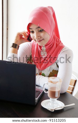 Young stylish muslim women talking on mobile phone in front of notebook at a cafe