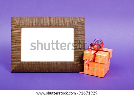 Wooden photo frame and orange gift box with red ribbon on purple background.