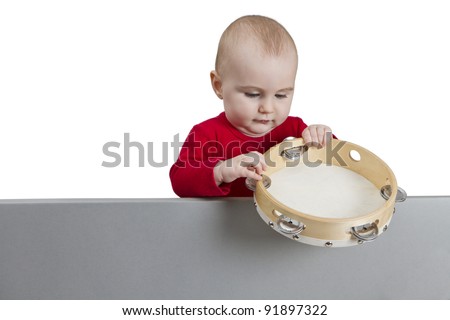 young child holding tambourine behind grey shield. isolate on white background