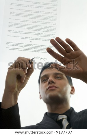 Young, serious businessman signing centract. Low angle view