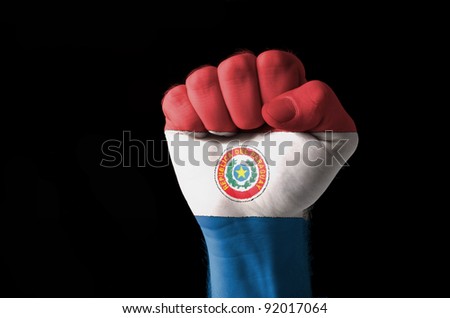 Low key picture of a fist painted in colors of paraguay flag