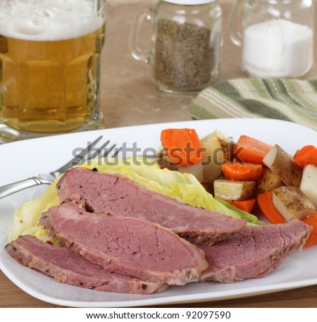Sliced corned beef and cabbage with vegetables on a plate and a glass of beer in background