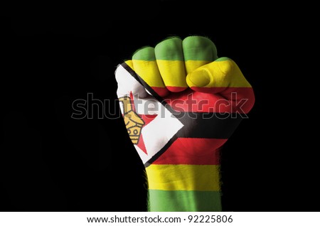 Low key picture of a fist painted in colors of zimbabwe flag