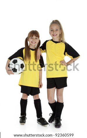 Full length front view of two young girls in soccer uniforms, holding soccer ball on white.