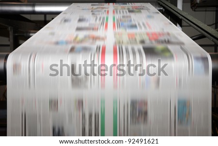 A large offset printing press running a long roll off paper over its rollers at high speed. Royalty-Free Stock Photo #92491621
