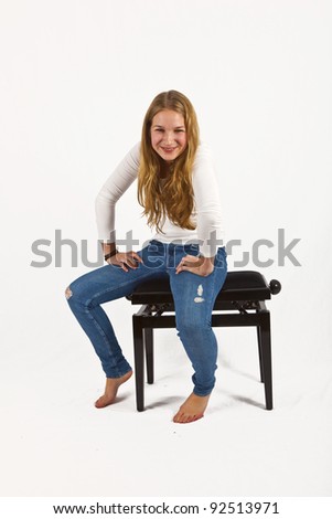 Full length portrait of happy beautiful girl sitting on a piano chair, isolated on white background