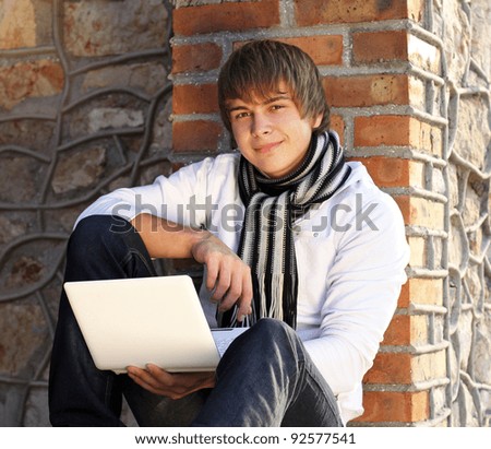 Young man with laptop leaning against the brick wall
