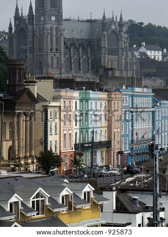 Cityscape of Cork, Ireland with a row of colorful buildings and an old, gothic stone church in the background.