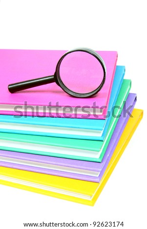 Magnifying glass on top of a stack of colorful books on white