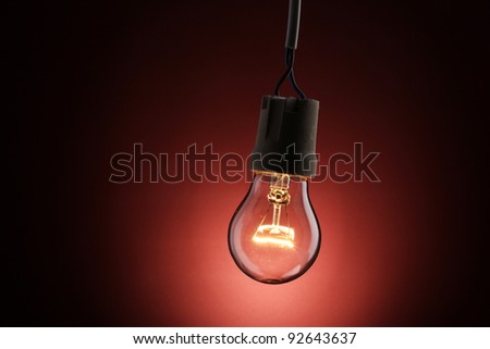 A lit light bulb on red background