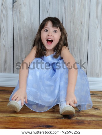 expressive little girl in dress sitting on floor with eyes and mouth wide open