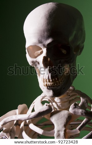 Sinister looking skull and shoulders of a skeleton emerging from the shadows against a green background