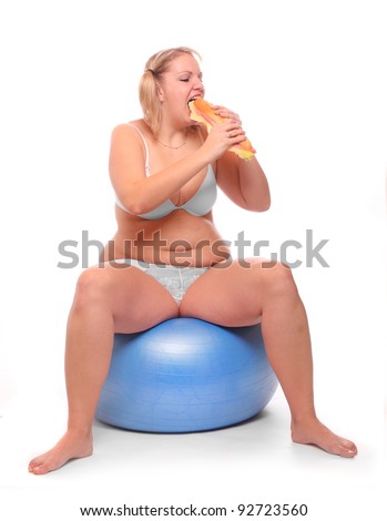 Funny picture of overweight woman sitting on a fitness ball eating big sandwich.