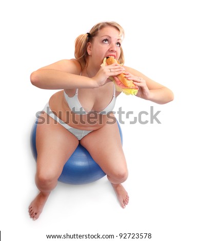 Funny picture of overweight woman sitting on a fitness ball eating big sandwich.