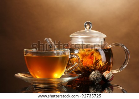 glass teapot and cup with exotic green tea on wooden table on brown background