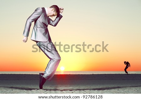 Business man in gray suit dancing at sunset at the beach.