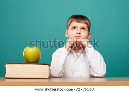 cheerful  little boy sitting at the table and looks up. School concept