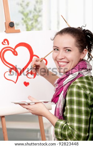 Love or Valentine day - concept image. Beautiful girl with brushes near easel, painting on canvas.