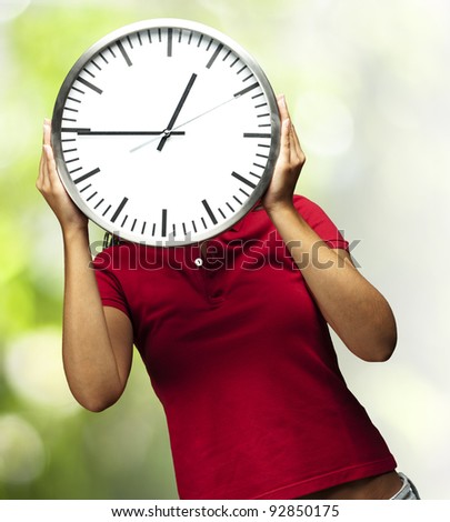 woman holding clock in front of head against a nature background