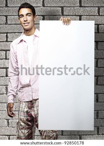 portrait of young man smiling and showing a banner against a bricks wall