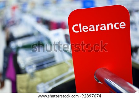A red sale clearance sign on rail of clothes in a shop