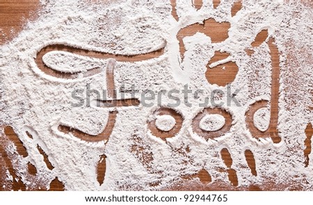 Flour Artwork With Food And Handprints, Fun background with the word FOOD and human handpints in scattered flour on a wooden tabletop.