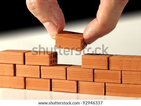 Two fingers put the last brick on the wall. Metaphoric scene Royalty-Free Stock Photo #92946337