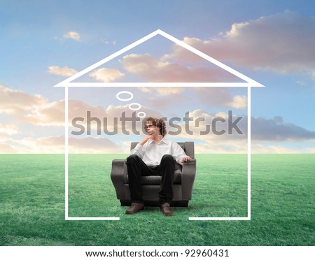 Young businessman with thoughtful expression sitting on an armchair surrounded by the shape of a house