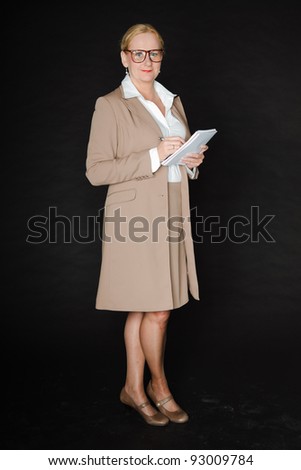 Studio portrait of senior blond woman wearing glasses in light brown suit and white shirt holding pen and paper isolated on black background