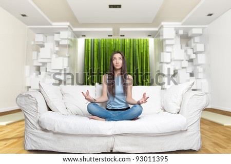 Young woman sitting on a sofa in the lotus position meditating in a zen environment Royalty-Free Stock Photo #93011395