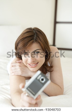 Young woman taking a picture while laying down on bed.