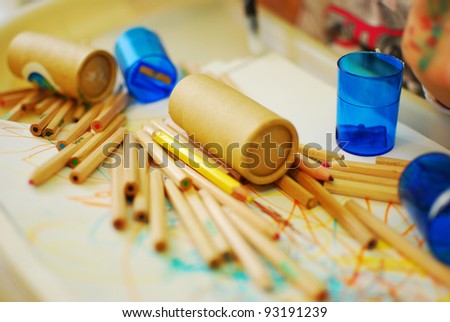 Colored pencils spread on a scribbled paper with pencil sharpeners around and pencil boxes