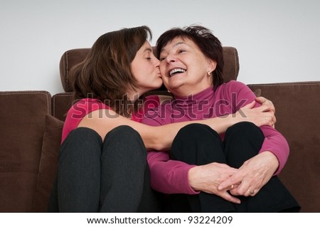 Portrait of daughter kissing happy senior mother sitting on sofa at home