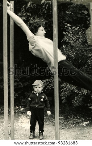 little boy stands near the horizontal bar, which swings teenager, Kursk, USSR, 1984 (very grainy image)