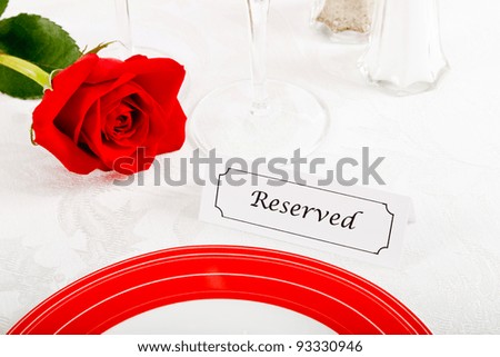 Close up of a romantic red and white place setting shows a reserved table at an elegant restaurant ready to celebrate an anniversary or Valentine's Day.