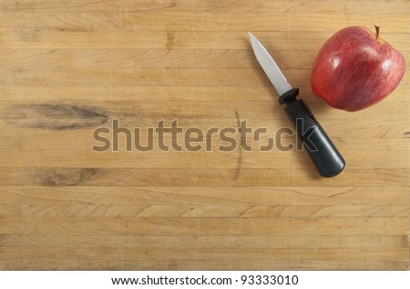 A red delicious apple sits next to a paring knife on a worn cutting board