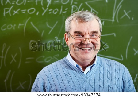 Portrait of aged teacher looking at camera with blackboard on background