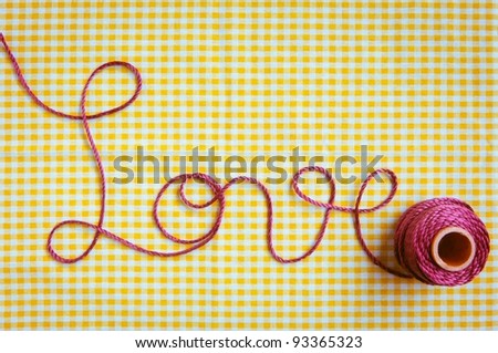 The word love drawn out with purple thread and a checked fabric background.