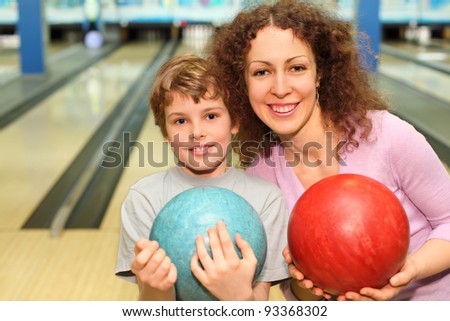 beautiful young mother and son keep red and blue balls in bowling club