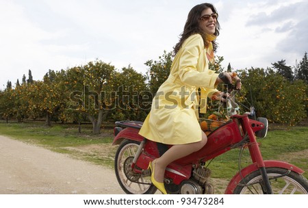 Sophisticated young woman on an old motorbike in an orange grove.
