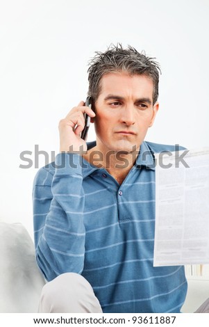 Man with cell phone and phone bill in living room