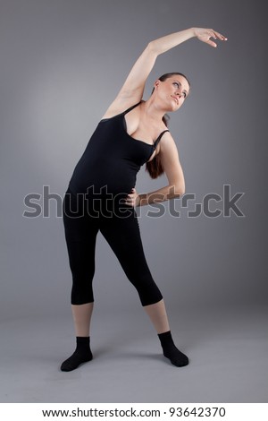 Pregnant woman doing gymnastic exercises on grey background.