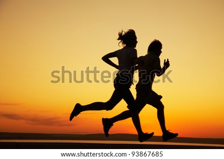 Young couple: man and  woman run together on a sunset on lake coast.  Silhouette. Royalty-Free Stock Photo #93867685