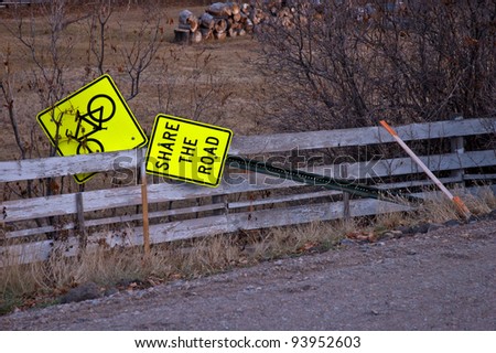 A road sign indicating the need to yield to bicycle traffic is seen lying against a fence near the shoulder of the roadway