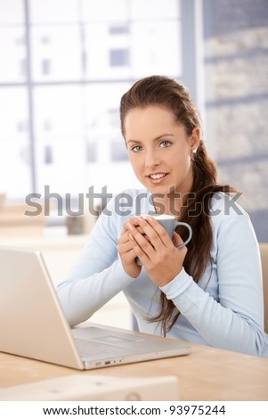 Attractive woman browsing internet at home, drinking tea, smiling.?